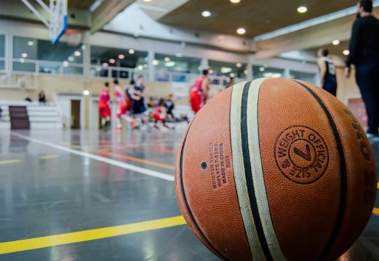 Minge de baschet pe terenul de joc, cu echipa Madmax Basketball Iași antrenându-se în fundal.